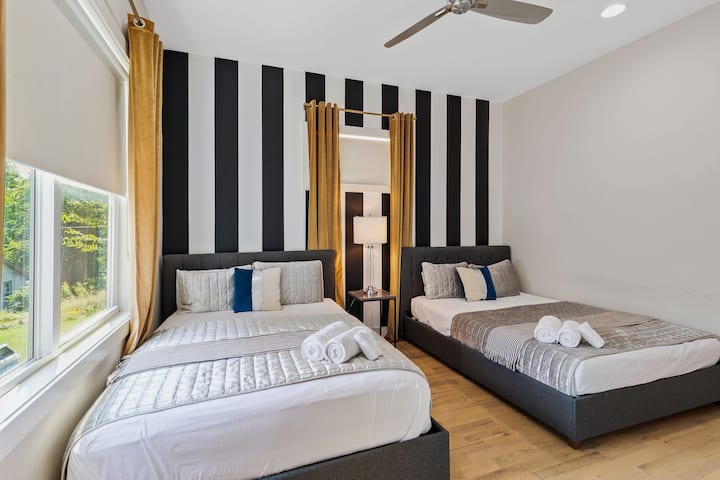 Bright bedroom with two queen beds, modern striped accent wall, ceiling fan, and natural light. Comfortable bedding and a clean design make this space ideal for friends or family traveling together.