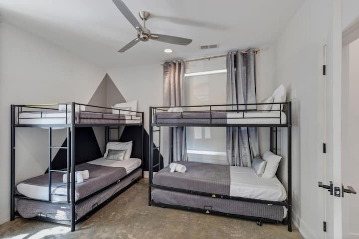 Large bunk room with multiple beds, ceiling fan, and natural light. Designed for groups with a comfortable layout, clean décor, and plenty of space for guests to sleep and recharge.