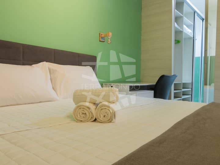 Quarto com cama queen, enxoval. O ambiente é climatizado com ar condicionado e possui área de trabalho com mesa e cadeira ergonômica, ideal para home office ou estudos durante a viagem.