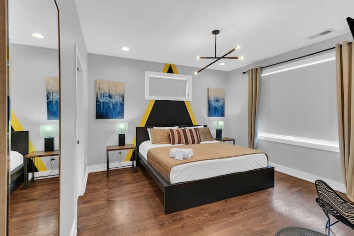 Stylish bedroom with king bed, smart TV, modern décor, and plenty of natural light. Designed for comfort with cozy bedding, clean lines, and a relaxing space to unwind after a full day out.