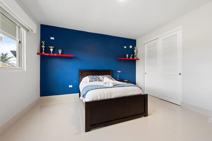 Un dormitorio moderno con detalles en azul intenso, una cama completa y una zona para trabajar. Incluye un baño privado con una combinación de ducha y bañera, perfecta para la comodidad y la conveniencia durante su estancia.