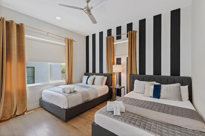 Bright bedroom with two queen beds, modern striped accent wall, ceiling fan, and natural light. Comfortable bedding and a clean design make this space ideal for friends or family traveling together.