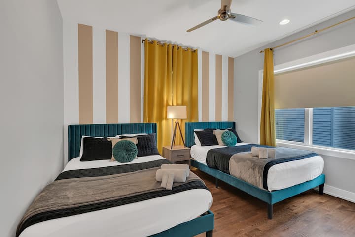 Bright bedroom with two queen beds, stylish décor, ceiling fan, and natural light. Comfortable bedding and a clean, modern design make this a great space for friends or family to relax and recharge.