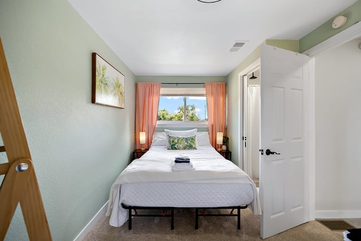 ห้องนอนบรรยากาศเขตร้อนมีเตียงคู่เต็มรูปแบบ 1 เตียงโคมไฟแบบสัมผัสพร้อมพอร์ตชาร์จ USB และห้องน้ำแบบแจ็คแอนด์จิล มีกระจกบานใหญ่และไม้แขวนเสื้อกำมะหยี่ในตู้เสื้อผ้าพัดลมเสริมผ้าห่มม่านสีเข้มในห้องและมู่ลี่ไร้สาย