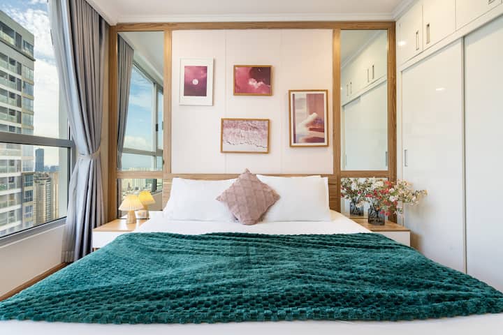 חדר שינה פתוח ומואר עם דלת זכוכית גדולה, נוף יפה לעיר. מיטת קווין סייז בגודל 1.6 מ'. מרחב מעוצב בקלות עם אמנות קיר, מדף ספרים וארון בגדים מרווח – מביאים תחושה נעימה ופרטית לחופשה.