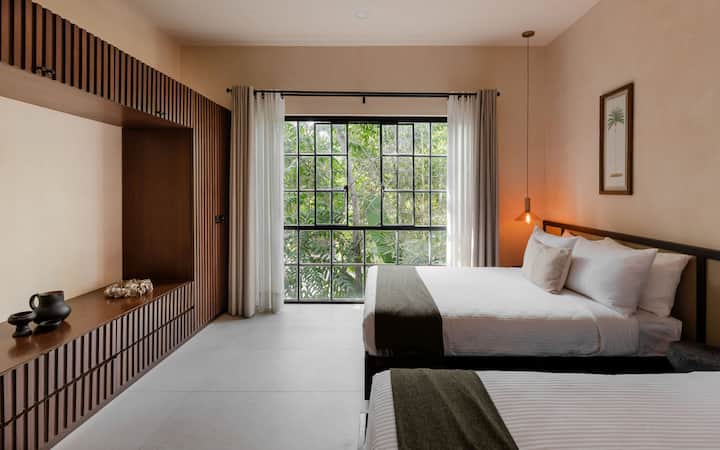 Amplio segundo dormitorio con dos camas tamaño queen, baño privado y vistas relajantes de exuberantes plantas tropicales.