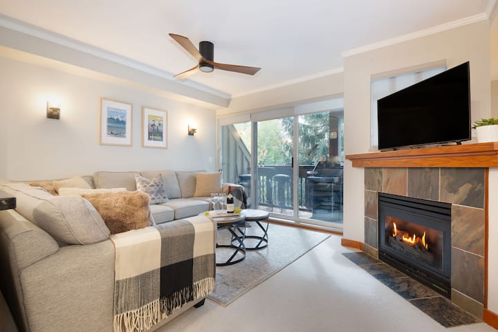 Otvorená obývacia izba s veľkou rozkladacou pohovkou, útulným kozubom a inteligentným televízorom.