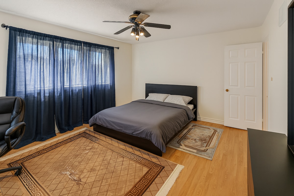 غرفة نوم مشرقة وواسعة تتميز بسرير مريح بحجم كوين ونافذة كبيرة مع ستائر تعتيم ومروحة سقف حديثة. مثالية لليالي المريحة والصباح الهادئ.