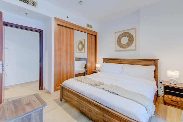 חדר שינה שני עם מיטת קינג סייז מעץ אגוז, שני שולחנות צד עם מנורות, ארון בגדים עם מראה, ציור בסגנון בוהו, ומיטה לבנה וצהובה.