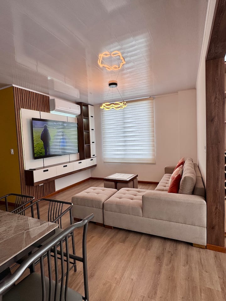 Dhoma e ndenjjes me divan në formë L-je, përfshin tavolinë kafeje dhe 4 stola puff, ka Smart TV, ajër të kondicionuar, grila automatike.