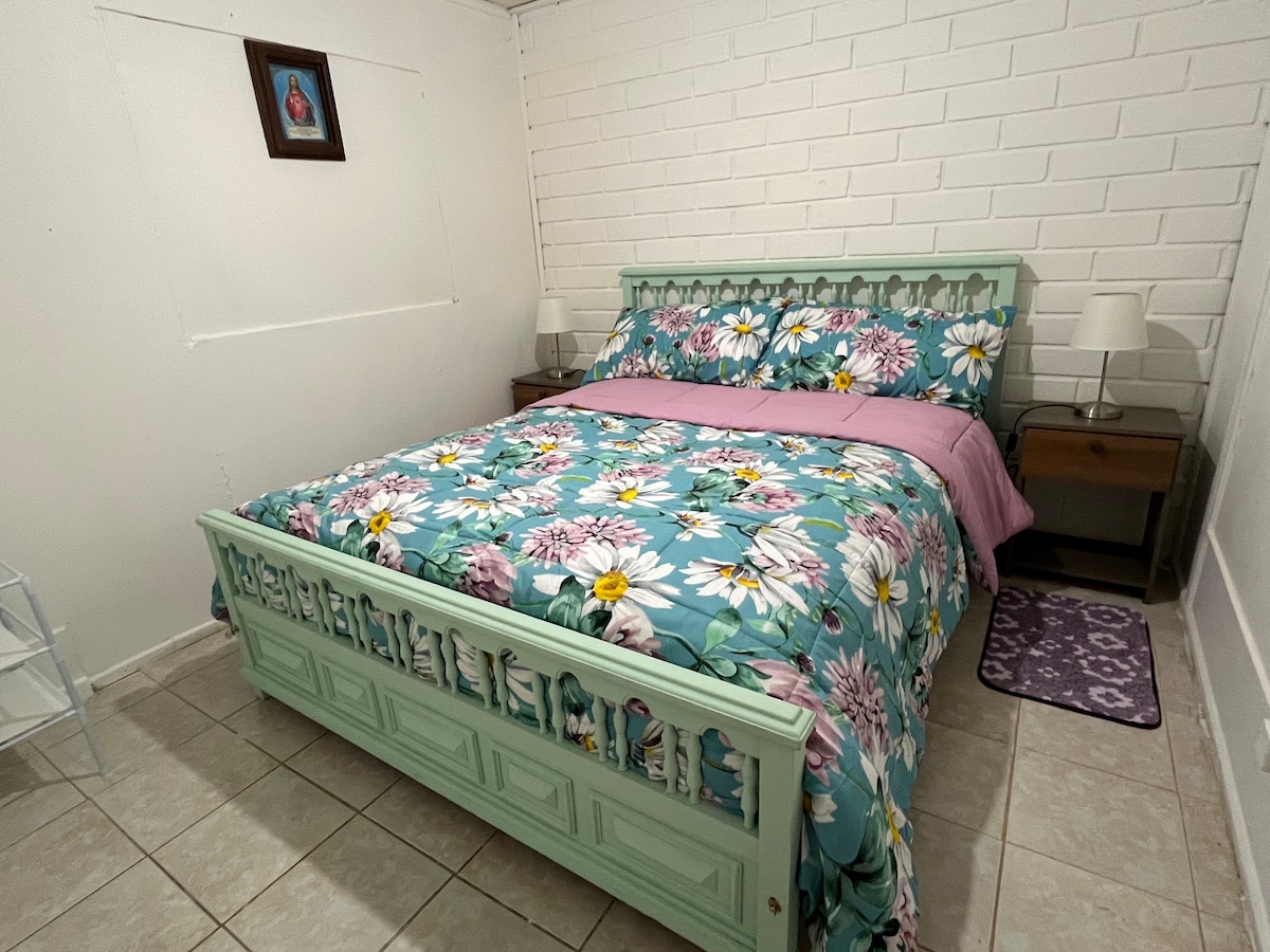 חדר עם מיטה זוגית, מנורות ליד המיטה, חיפוי מיטה ומתלה לבגדים.