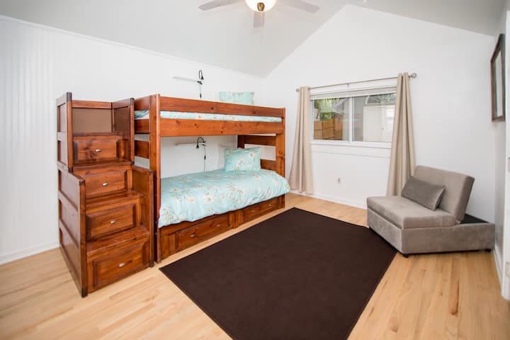 Голема спална соба со двоен кревет на спрат и пристап до скалите до најгорниот спрат.  Секој кревет има своја полица и лично светло. Сивиот стол се претвора во друг кревет погоден за мало дете. Затемнете ги завесите на двата прозорци.