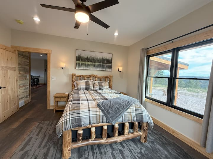 Táto útulná spálňa má rustikálnu posteľ z drevených trámov, teplé drevené prvky a veľké okná s krásnym výhľadom na Black Hills. Jemné osvetlenie a prírodné tóny vytvárajú pokojné útočisko ideálne na odpočinok a relax.