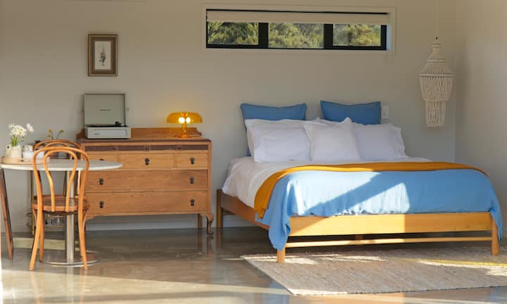 Un estudio luminoso y aireado con una cómoda cama tamaño king y puertas que se abren completamente y dejan entrar el jardín. Las sábanas suaves, las texturas naturales y la luz cálida durante todo el día crean un espacio tranquilo para despertarse o relajarse por la noche