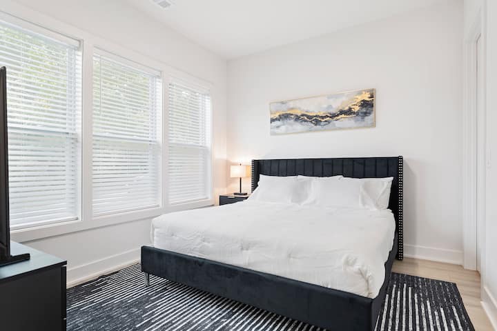 Елегантна гостинска соба со удобен брачен кревет (king size), модерна црна рамка и мека бела постелнина. Големите прозорци го исполнуваат просторот со природна светлина, создавајќи смирено чувство како во бутик хотел, совршено за опуштање.