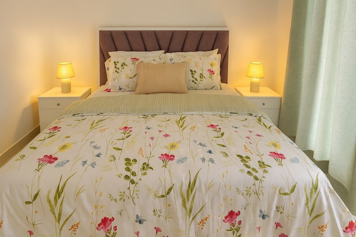 Habitación luminosa y tranquila con una acogedora cama tamaño queen, aire acondicionado, iluminación suave y ropa de cama floral. Disfruta de un balcón privado con vistas relajantes y un armario espacioso para un fácil almacenamiento. Un espacio tranquilo y acogedor perfecto para relajarse.