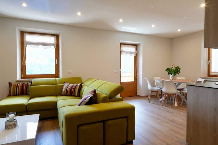 סלון מואר עם מטבח, יש בו ספה פינתית נוחה, טלוויזיה עם מסך שטוח וחלונות גדולים שמעניקים הרבה אור טבעי. ריהוט מודרני ופרטים מוקפדים יוצרים אווירה חמימה ומזמינה.