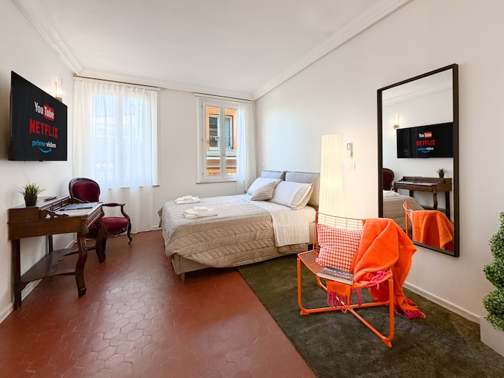 Un dormitorio con vistas a los tejados del centro de Módena. Equipada con aire acondicionado, un moderno sillón, un escritorio antiguo para estudiar o trabajar, una cama doble y un televisor inteligente 4K con conexión a Internet.