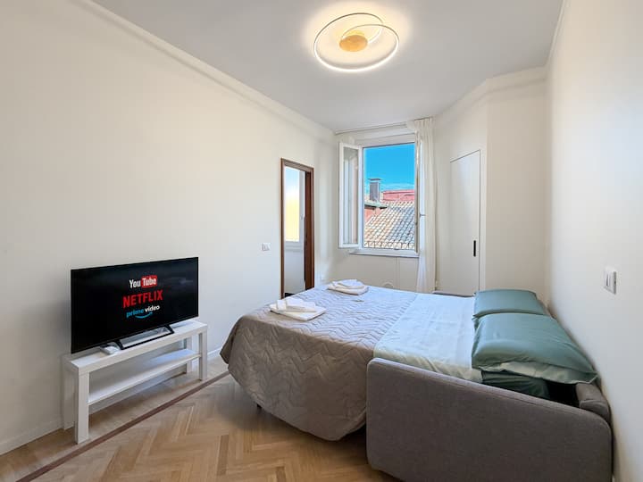 Dormitorio con vistas a los tejados del centro de Módena y baño privado en la habitación. Equipado con aire acondicionado, sofá cama y Smart TV 4K con conexión a Internet.