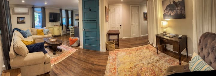 В дневната синята врата е към стълбището и е заключена.  Може да се заключи от ваша страна с помощта на болта.  Банята е зад дясната врата на далечната стена.  Подноси за телевизор и сгъваеми столове в килера вляво от бюрото.