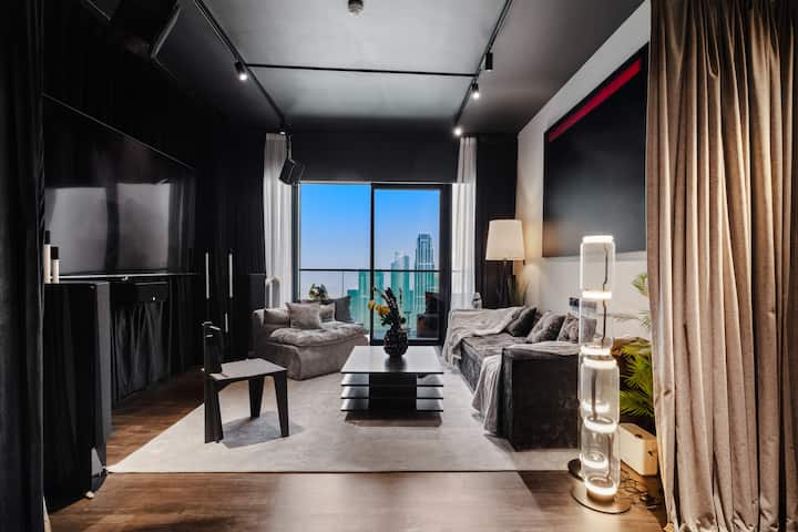 Сместете се во дневна соба во црна боја каде што просторот е исполнет со плишани седишта, меки ламби и елегантна маса. Прозорците од подот до таванот го врамуваат градот, додека софистицираниот декор и амбиенталното осветлување создаваат непречено и пријатно место за да се опуштите.