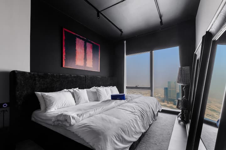 Во спална соба со црна тема, ѕидовите во боја на јаглен се спојуваат со меката дневна светлина која се излева низ високите прозорци, создавајќи смирено и тивко чувство. Свежото постелнино и погледот ви нудат модерно катче за да се сместите и да се опуштите.