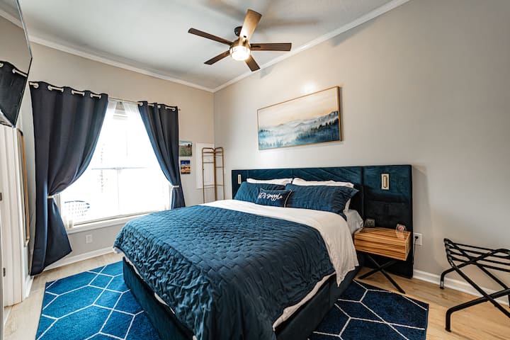 Chumba cha kulala cha mfalme chenye mwangaza na matandiko ya kifahari, sanaa ya mlima na mapazia ya kuzuia mwanga kwa ajili ya usingizi wa usiku wa kupumzika.