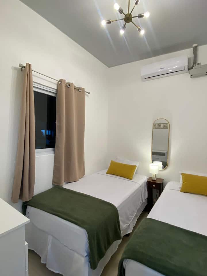 Izba s dvoma oddelenými posteľami, klimatizáciou, nočným stolíkom a multifunkčnou komodou.