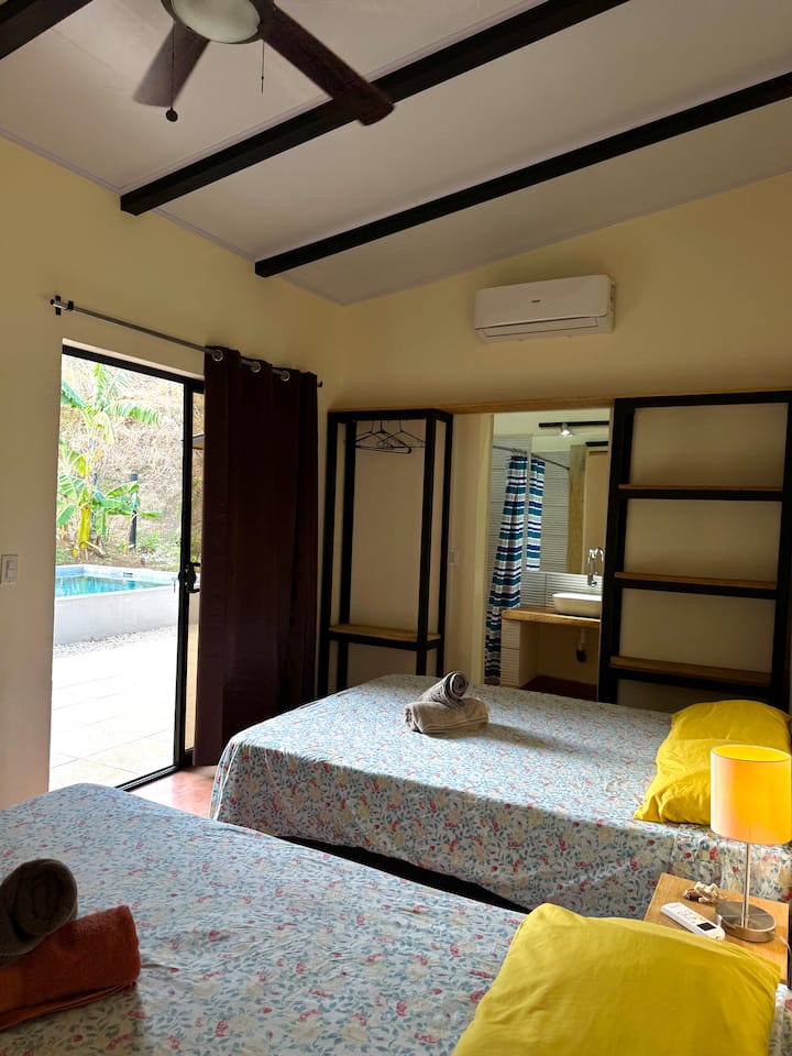 Cómoda habitación equipada con dos camas dobles, con baño privado, aire acondicionado y vista a la piscina. 