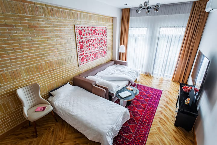 ห้องนั่งเล่นกว้างขวางสามารถรองรับได้สองคนอย่างสบายๆ — คนหนึ่งนั่งบนโซฟาหรู อีกคนหนึ่งนอนบนเตียงที่สบาย ที่พักนี้เหมาะสำหรับการพักผ่อนและยามเย็นที่เงียบสงบพร้อมแสงไฟที่น่ารื่นรมย์และบรรยากาศที่อบอุ่น