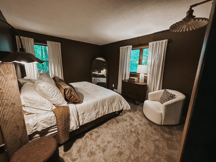 Pokojná spálňa s posteľou veľkosti King a výhľadom na les a golfové ihrisko, luxusná posteľná bielizeň a útulné sedačky – ideálne na pobyty a relaxačné pobyty v štýle chaty.