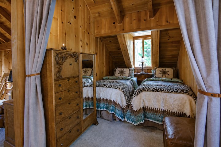 Cozy upstairs Twin Star Loft with two twin beds and a curtained entry. A warm, Western-inspired sleeping space with soft linens, star quilts, and rustic cabin charm.