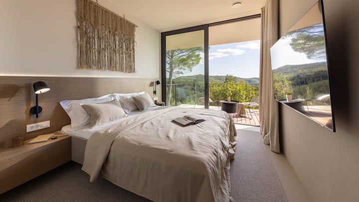 Amplio dormitorio principal con cama tamaño king y ventanales de piso a techo, llenando la habitación de luz natural. Despiértate con serenas vistas a viñedos y bosques, combinando lujo, comodidad y tranquilidad en un retiro pacífico.