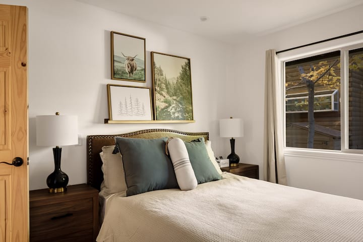 Habitación temática de montaña con mesitas auxiliares, armario completo, televisión y ropa de cama cómoda.