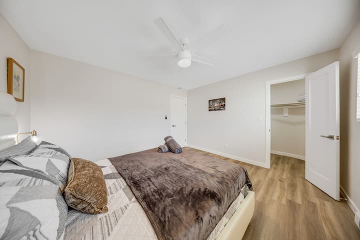 Удобна спална соба со голем кревет со шарени перници и кадифено кафеаво ќебе. Собата има ѕидови во светла боја, тавански вентилатор и дрвен под. Отворената врата открива плакар, што придонесува за пространото чувство.