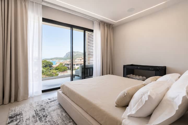 Golfo Aranci'deki AZULIS Athos Villa'da çift kişilik king boy yatak, projektör, yumuşak perdeler, teras kapıları, isteğe bağlı bebek karyolası, havlular ve deniz, körfez ve dağ manzaraları olan modern ana yatak odası.