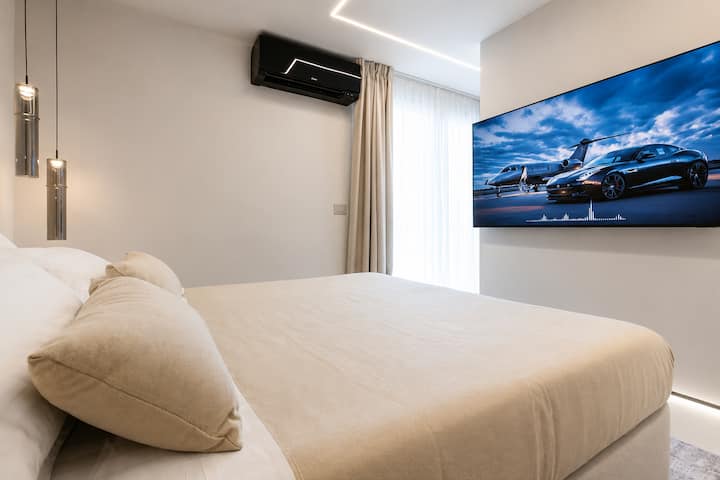 Golfo Aranci'deki AZULIS Athos Villa'da yatak, duvara monte akıllı TV, klima ünitesi, sarkıt lambalar, perdeler ve LED tavan aydınlatması bulunan modern yatak odası.