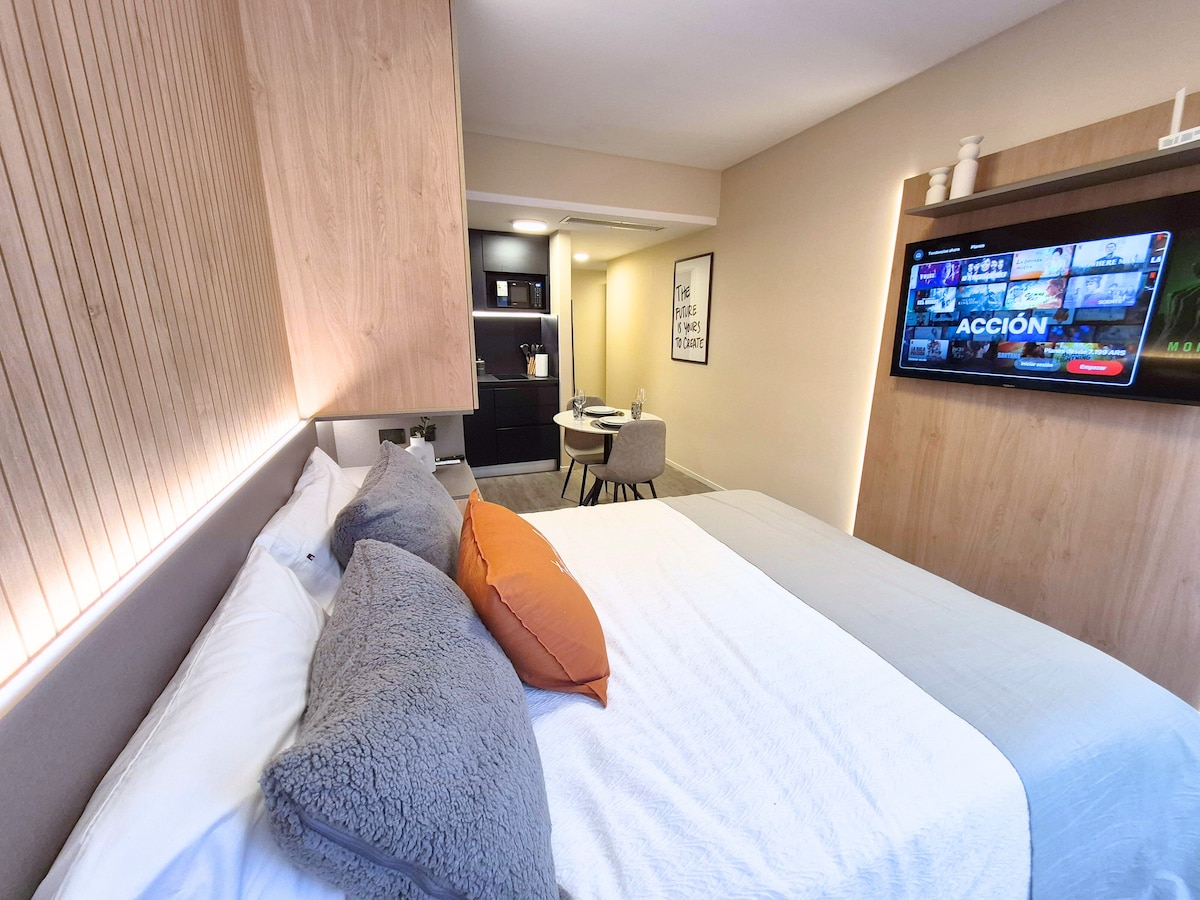 This image best represents the stay because it clearly shows a private interior bedroom with a bed, work/dining area, and kitchenette in one bright, understandable layout. It feels presentable, spacious enough for a booking thumbnail, and a