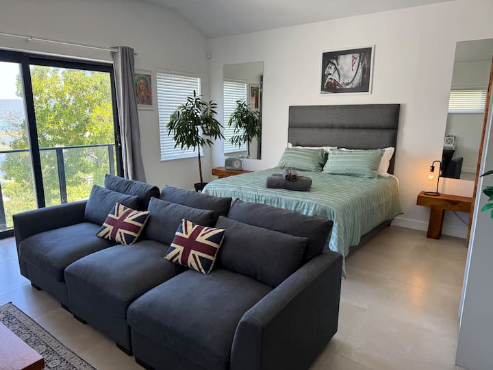 Amplio apartamento estudio de lujo con sala de estar, dormitorio y barra de desayuno con sillas de cuero de estilo respaldo alto. Impresionantes vistas de Knysna Heads y la laguna desde tu propio balcón de Julieta
