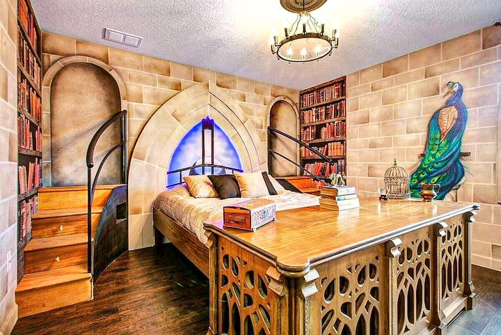Dumbledore's hand-carved desk anchors the foot of the bed. Gothic stone arches, a blue cathedral window, a hand-painted peacock mural shimmering on the far wall. Fall asleep in the Wizard's Study feeling centuries away from real life.