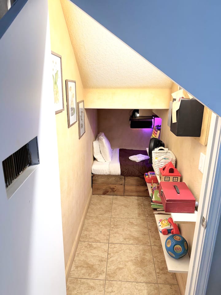 A small glowing door. A cluttered closet — toys, pipes, Hogwarts letters. Keep walking. The back opens into a full kids bedroom, snowy owl lamp, TV and gaming system. Harry never had it this good.