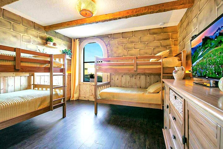 The Honeylight Suite. Honey-toned wooden bunks, soft golden light through an arched window, a big-screen TV on the dresser. Hufflepuff always made the most welcoming room — and this one proves it.