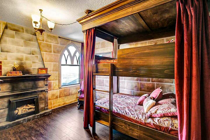 ✨ High Castle Suite: A regal, storybook retreat featuring a custom wood bunk bed draped in deep red velvet curtains and brick-style walls.