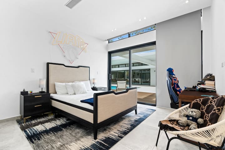 Štýlová spálňa s priamym prístupom k bazénu, ktorá ponúka modernú manželskú posteľ, útulný kútik na sedenie a elegantné dizajnové prvky. Priestor je plný prirodzeného svetla, ktoré vytvára jasnú a uvoľnenú atmosféru. 