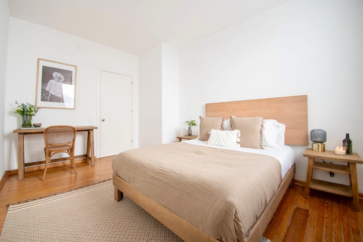 Ამ მშვიდ საძინებელში არის მინიმალისტური დიზაინი ხის თბილი ტონებითა და რბილი კრემისფერი ქსოვილებით. Ჩარჩოში ჩასმული პორტრეტი და კურირებული დეკორი დახვეწილ, სარედაქციო შტრიხებს ქმნის.