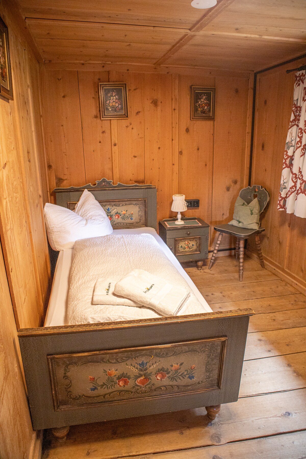 Pequeña habitación individual con cama rústica, armario y cuadros tradicionales. Perfecto para la tranquilidad y la recreación.