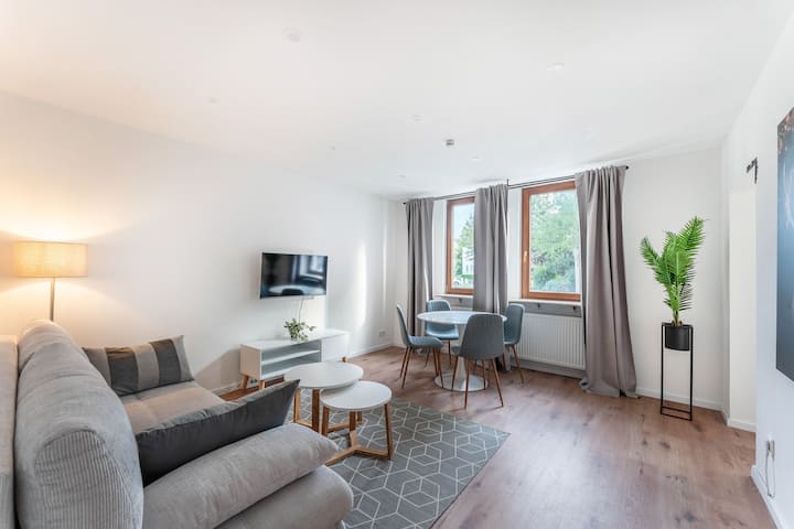 Acogedor salón-comedor con sofá cama para dos personas, luz cálida, televisor inteligente, mesa de comedor y cortinas opacas, perfecto para relajarse o reunirse.