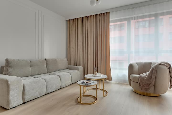 Una amplia sala de estar con sofá cama y grandes ventanales proporciona un descanso cómodo en un interior luminoso y lleno de luz. Un elegante comedor con una mesa de mármol y sillas de terciopelo completa el cuadro.