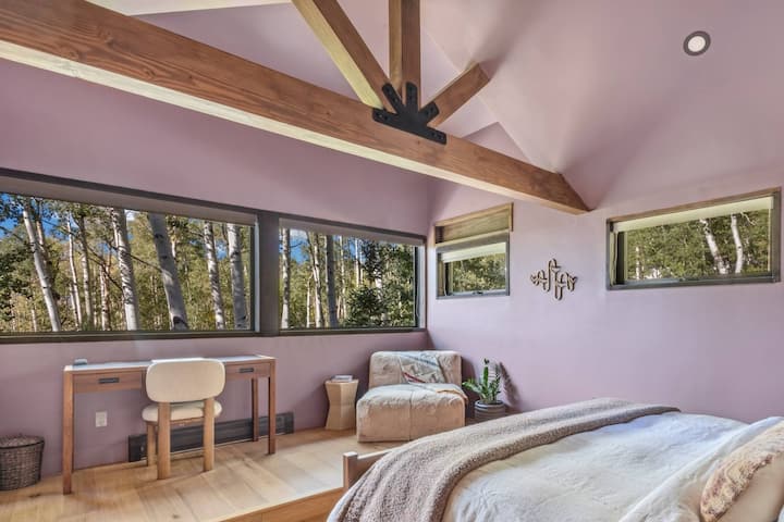 Aspen Room from the desk side — the windows that make this room, the sheepskin reading chair, and the vaulted beam overhead. Blackout shades, air purifier, and humidifier.