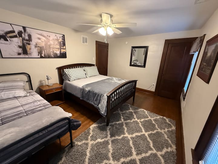 Quarto grande com cama queen size, bem como uma cama de solteiro. Grande closet, cômoda e mesa de cabeceira com lâmpada. A luminária tem porta de carregamento